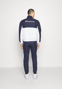 Navy and white tracksuit featuring a zip-up jacket and matching pants with side stripes, made from smooth fabric, with logo detail on the back.