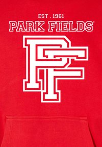 Piros kapucnis pulóver, amelyen egy nagy fehér grafikán az összefonódott "PF" betűk láthatók, fölötte a "PARK FIELDS" és az "EST. 1961" felirattal. Puha tapintású.