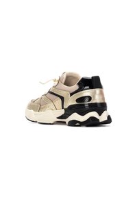 Zapatillas gruesas con un upper metálico dorado y acentos texturizados, suela negra y paneles de malla beige. Cordones y recortes laterales visibles.