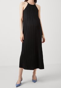 Czarna pleciona sukienka halter o swobodnej sylwetce. Podkreślona błyszczącym wykończeniem i noszona z jasnobłękitnymi, spiczastymi sandałami na obcasie.