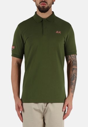 Polo shirt verde oliva con colletto, maniche corte, logo in rilievo sul lato sinistro del petto e testo ricamato sulla manica destra.