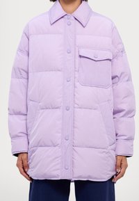 Chaqueta acolchada en lavanda claro con cierre de botones, gran cuello y un bolsillo en el pecho. Presenta una textura suave y brillante, así como un diseño acolchado.