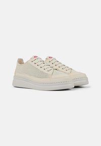 Sneakers beige chiaro con pannelli in rete, punta rotonda e suola piatta in gomma bianca. Presentano lacci tonali e accenti rossi con il logo sulla linguetta.