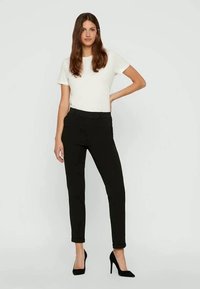 Calças pretas à medida com um corte justo, cintura alta e uma textura suave, combinadas com uma blusa branca de mangas curtas e sapatos de salto alto pretos.