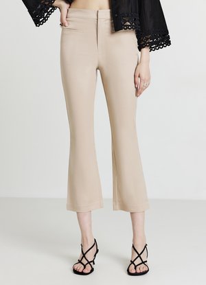 Pantalon beige évasé ajusté avec une texture lisse et des poches avant, associé à des sandales noires à talons hauts et à lanières.