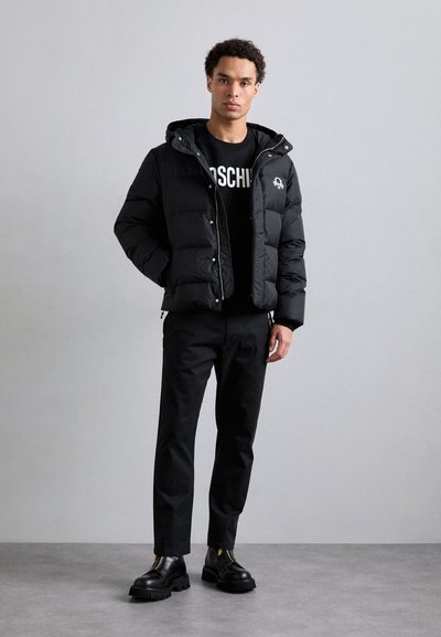 Sort dunjakke med hætte, prydet med en quiltet design. Bæres over en sort sweatshirt med trykt tekst, kombineret med slanke sorte bukser og kraftige støvler.