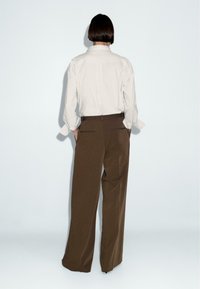 Camicia grigia chiara con colletto e maniche lunghe, abbinata a pantaloni marroni a gamba larga a vita alta. Tessuto liscia, design minimalista, senza motivi visibili.