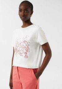 Weißes T-Shirt mit rotem Hummer-Graphic, kurze Ärmel, Rundhalsausschnitt; kombiniert mit korallenfarbenen Hosen. Glatter Stoff, lässiger Schnitt, minimales Design.