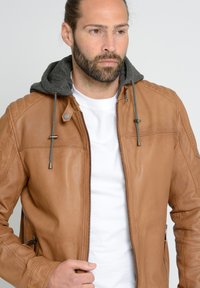 Braune Lederjacke mit grauem Kapuzen, Reißverschluss vorne, zwei Seitentaschen und kontrastierenden Nähten. Glatte Textur und taillierter Schnitt.