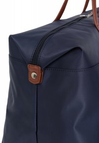 Sac en nylon bleu marine avec fermeture éclair, doté d'accents en cuir brun et d'un bouton pression sur le côté. Texture lisse, design rectangulaire.