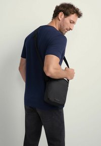 Czarna torba na ramię wykonana z trwałego materiału. Prostokątny kształt z gładką fakturą i regulowanym paskiem. Minimalistyczny design z subtelnym logo.