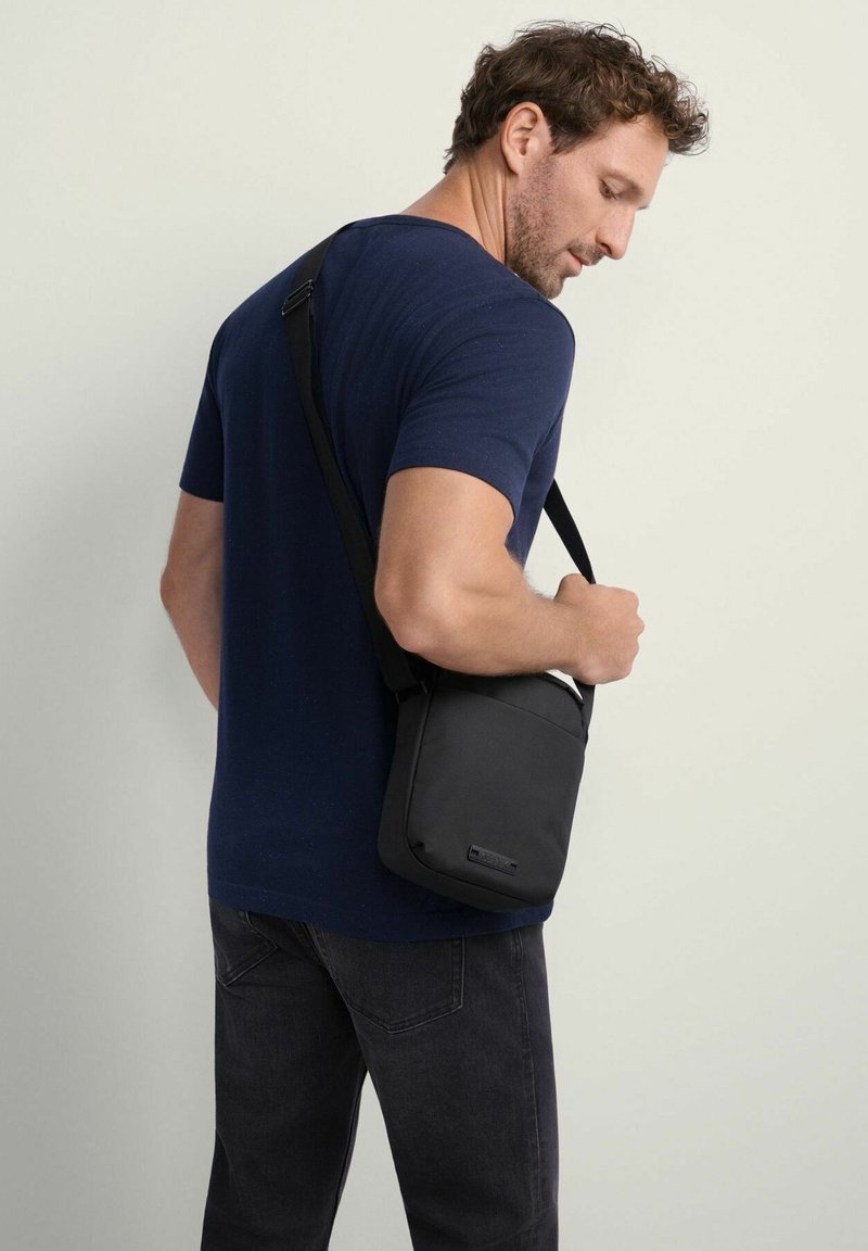 Czarna torba na ramię wykonana z trwałego materiału. Prostokątny kształt z gładką fakturą i regulowanym paskiem. Minimalistyczny design z subtelnym logo.