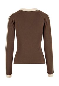 Ruskea pitkähihaisen paita, jossa on tiukka muotoilu. Koristeena kermanvärisiä yksityiskohtia kauluksessa ja hihansuiden reunassa. Sujuva pinta, uritettu kangas.