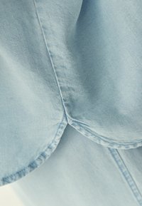 Gros plan sur un tissu bleu clair avec des coutures visibles, montrant la texture et les bords incurvés du matériau.
