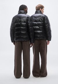 Čierne nadýchané bundy s lesklým povrchom, s horizontálnym prešívaním, vysokými goliermi a v kombinácii s voľnými hnedými nohavicami.