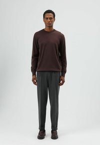 Chemise marron à manches longues avec un col rond, associée à un pantalon gris taille haute et des mocassins marron. Design simple et ajusté.