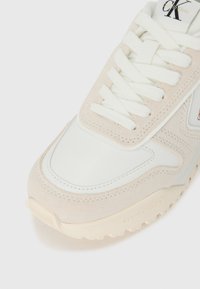 Sneaker bianco e rosa chiaro realizzato in materiali scamosciati e in pelle, con suola testurizzata e design con lacci. Dettaglio del logo presente sulla linguetta.