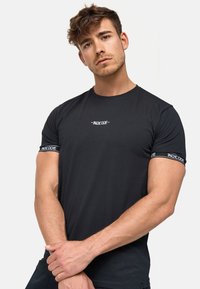 T-shirt en coton noir avec des manches courtes, un col rond et un logo texturé imprimé sur la poitrine et l'ourlet de la manche.