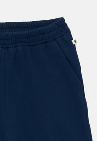 Dunkelblaue Sweatpants mit elastischem Bund, seitlichem Taschen und einem kleinen weißen Etikett mit einem schwarzen Stern auf der rechten Seite.