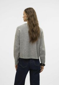 Suéter gris recortado con textura acanalada, sutiles rayas, escote redondo y mangas largas, combinado con jeans de mezclilla oscuros.