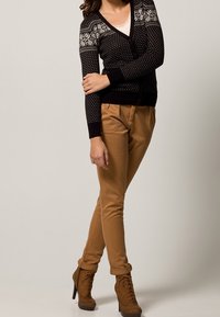 Svart kofta med vita mönster, parat med beige byxor. Bruna ankelstövlar med snördetaljer. Outfiten visar upp kontrasterande färger och texturer.