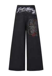 Schwarze weit geschnittene Jeans mit aufwendiger, mehrfarbiger Stickerei eines Drachen am linken Bein und weißem Text am Bund.