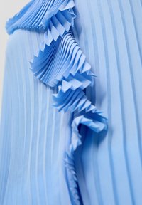 Lichtblau plissé stof met een gerimpelde rand, met verticale strepen en een zachte textuur in het materiaal.