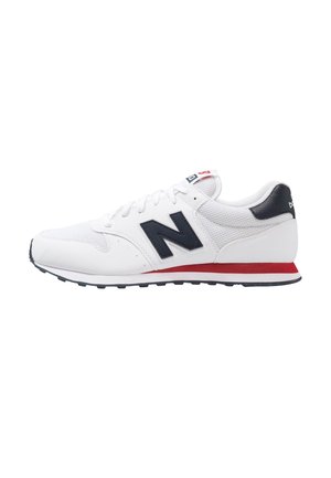 Witte sportschoen met zwart "N" logo, zwarte hielpatch, rode streep op de zool en witte veters op een platte zwarte buitenzool.