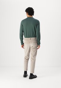 Zeleni dukserica dugih rukava u kombinaciji sa svijetlosivim tapered hlačama koje imaju elastičnu struk i stražnji džep; crne cipele završavaju outfit.