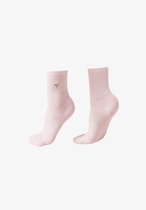 Chaussettes rose pâle côtelées avec un petit visage de chien blanc brodé sur le côté extérieur d'une chaussette, portées sur des pieds inclinés.