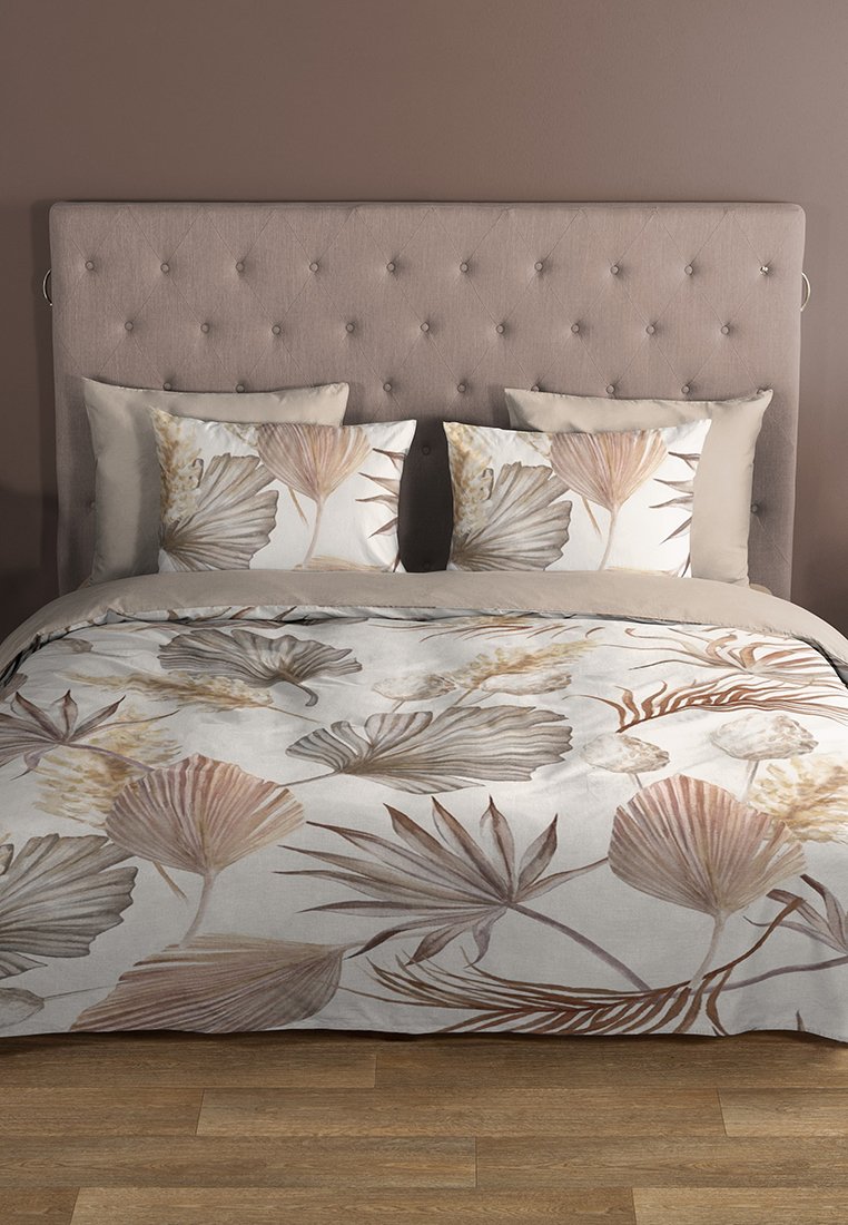 Juego de cama con patrones de hojas botánicas en tonos suaves de beige y marrón, textura acolchada, acompañado de almohadas beige sólidas, sobre un cabecero capitoné.