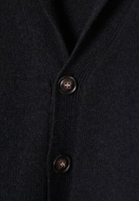 Jūras spēku zilas vilnas kardigāns ar faktūru, dziļu V veida izgriezumu un trim brūniem pogām priekšpusē, kas kalpo aizdarei.