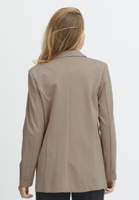 Beige, testreszabott blézer, struktúrált dizájnnal, egysoros gombokkal, sima textúrával, hátsó hasítékkal és kontrasztos varrásokkal.