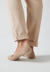 Chaussettes basses beiges avec une texture douce, présentant un design à bout rond et un talon sans couture. Les pantalons sont retroussés au niveau des chevilles.