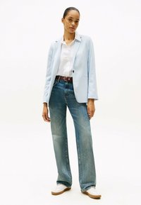 Blazer azzurro chiaro, camicia bianca, jeans blu a vita alta. Dettagli notevoli includono una cintura marrone e sneakers bianche con suole beige.