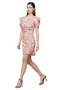 Blumendruckkleid in Hellrosa mit roten und grünen Akzenten, mit Puffärmeln und taillierter Silhouette. Getragen mit roten Riemenabsätzen.