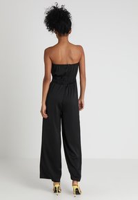 Combinaison noire sans bretelles avec une taille cintrée et des pantalons à jambes larges. Texture lisse ; se ferme par une fermeture éclair au dos et a une taille élastique.