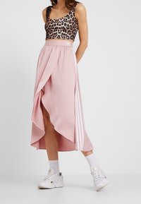 Leopardmönstrad crop top, rosa kjol med asymmetrisk fåll, vita detaljer med tre ränder, kombinerat med vita sneakers och strumpor.