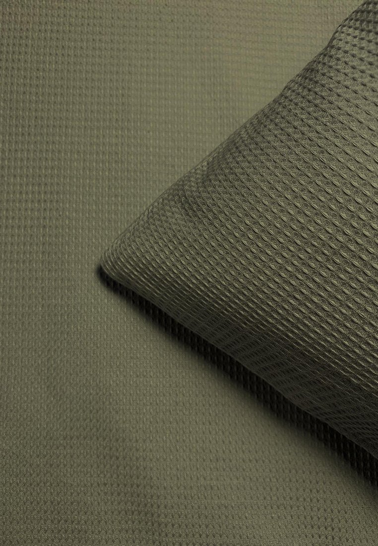 Texturiertes olivgrünes Gewebe mit einem erhabenen Muster; eine passende Kissen-Ecke ist leicht überlappt und zeigt das gleiche Material und die gleiche Farbnuance.