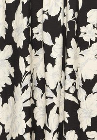 Tissu noir avec un grand motif floral en blanc et gris clair montrant des feuilles et des fleurs dans une texture fluide et drapée.