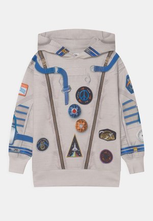 Sweat à capuche pour enfants beige avec des patchs à thème spatial, des fermetures éclair imprimées, des bretelles bleues et une capuche avec des accents bleus et blancs.