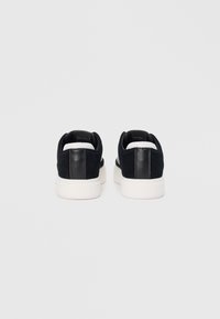 Sneaker neri in suede e pelle con suola in gomma bianca, caratterizzati da una texture liscia e un design minimalista. Vista posteriore che mostra una silhouette elegante.