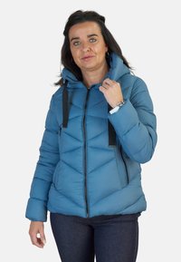 Chaqueta de plumas azul claro con capucha, con cierre frontal de cremallera, acentos de tiras negras y textura de acolchado en chevrón. Diseño casual.