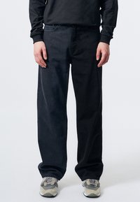 Jeans de mezclilla negra con un corte relajado, que cuentan con una cintura de altura media, cinco bolsillos y un diseño de pierna recta. Combinados con zapatillas grises.