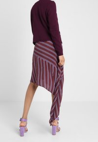 Lila stickad jacka, asymmetrisk randig kjol i vinröd med vita och lavendelfärgade linjer, tillsammans med lavendelfärgade klacksandaler.