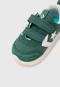 Sneaker in tela e suede verde con logo a stella bianca, fibbie a Velcro regolabili e suola in gomma di colore chiaro. Tessuto testurizzato e dettagli di cucitura.