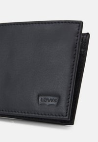 Portefeuille en cuir noir avec une texture lisse et des coutures subtiles. Présente un logo Levi's en relief dans le coin. Design simple et plié.
