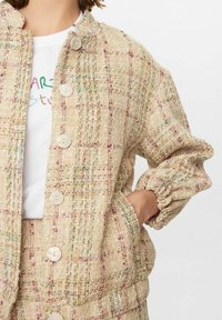 Veste en tweed avec un tissage texturé en beige et fils multicolores. Dotée de grands boutons et de poignets élastiqués ; comprend des poches latérales.