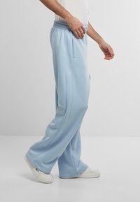 Light blue sweatpants with a relaxed fit, elastic waistband, and side pockets. Smooth texture and stitched details along the seams.