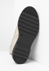 Beige leren laars met een zwarte rubberen zool, voorzien van horizontale groeven voor grip en een zijrits voor gemakkelijke toegang.